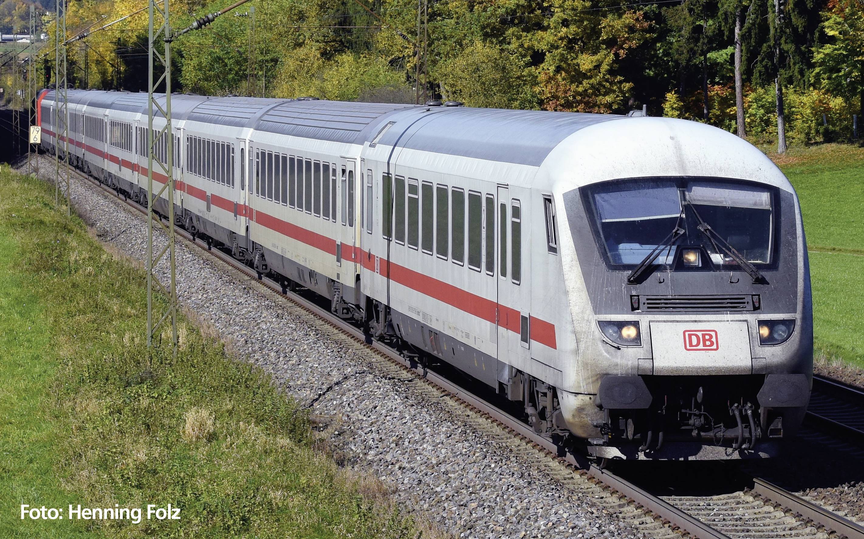 Červeno-biely diaľkový vlak Nemeckých železníc (Deutsche Bahn) jazdí po železničnej trati cez zelenú, zalesnenú krajinu.