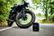 Čierna motorka stojí na ceste lemovanej stromami. V popredí je čierna taška s oranžovým logom 'OSRAM'.