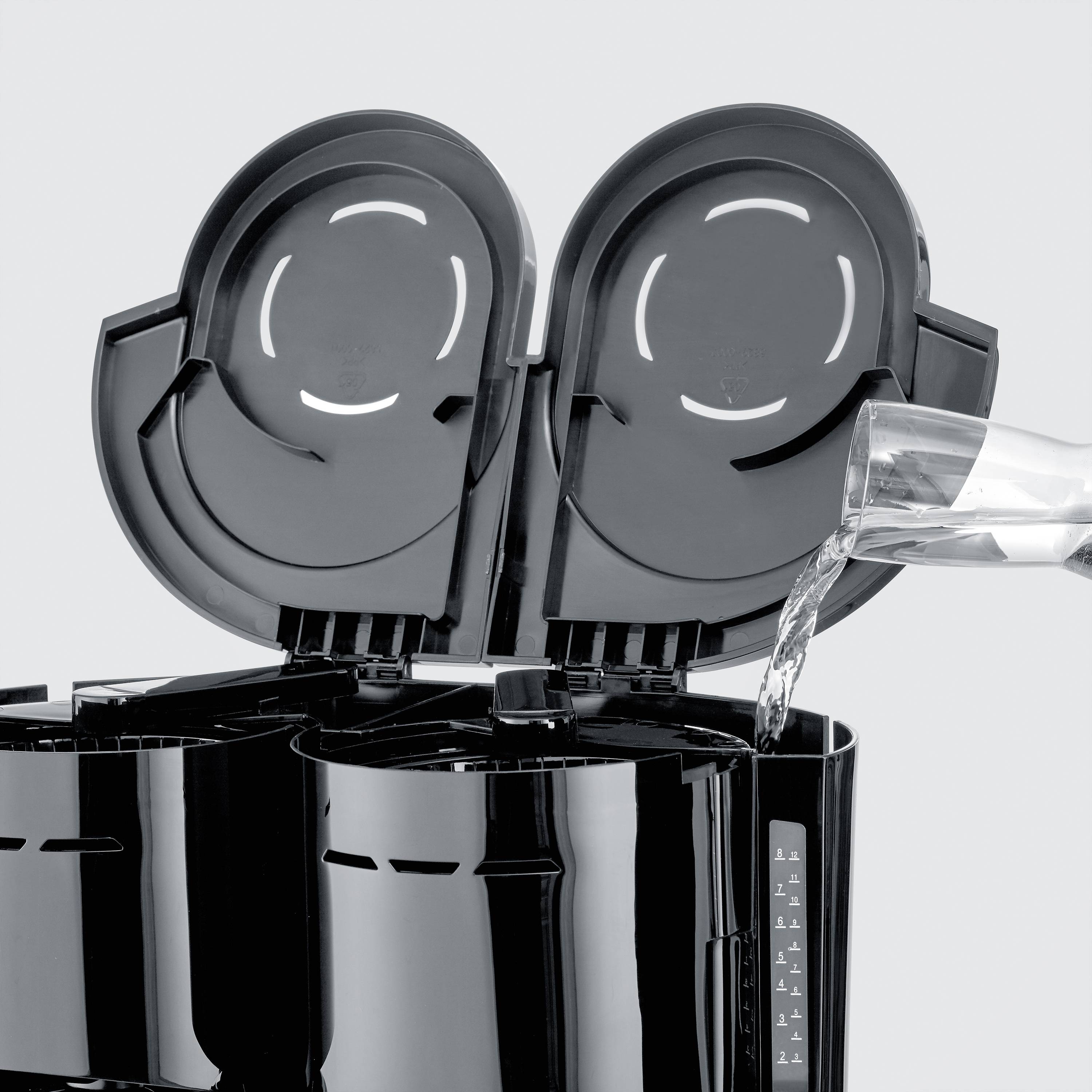 Kávový prístroj sa napĺňa vodou. Veko je otvorené a prúd vody tečie do vodnej nádrže.