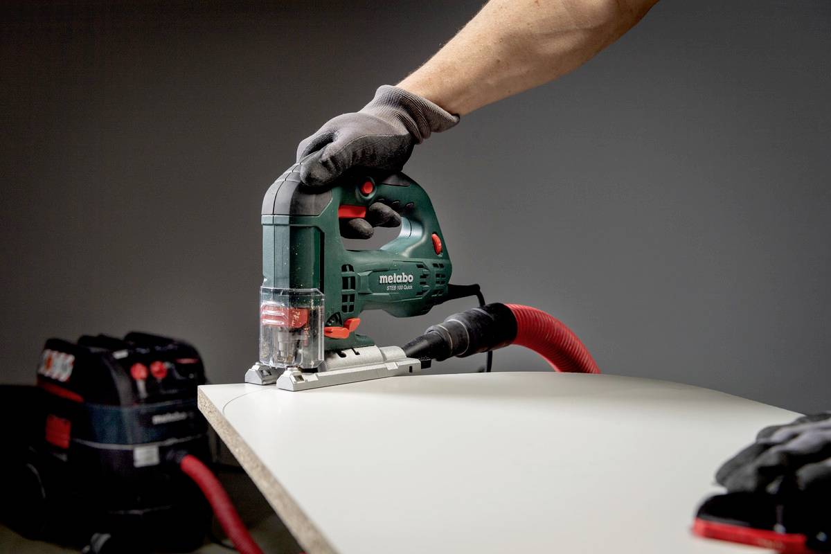 Osoba používa priamočiaru pílu pripojenú k vysávaču, aby minimalizovala prašnosť pri rezaní dreva.