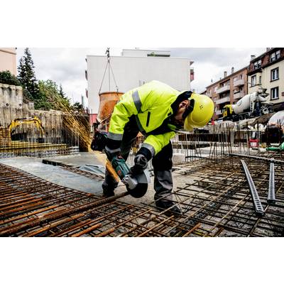Robotník v ochrannom oblečení rezá oceľové tyče na stavenisku. V pozadí sú viditeľné budovy a stavebné stroje.
