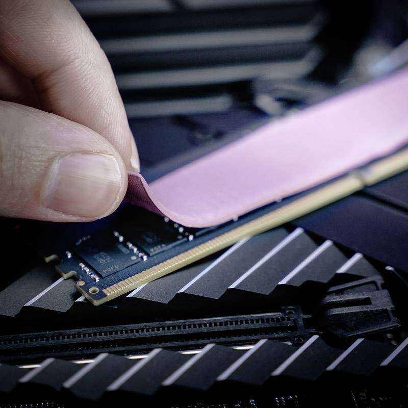Ruka opatrne odstraňuje ochrannú fóliu z pamäťového modulu RAM v počítači, ktorý je vidieť v detailnom zábere.