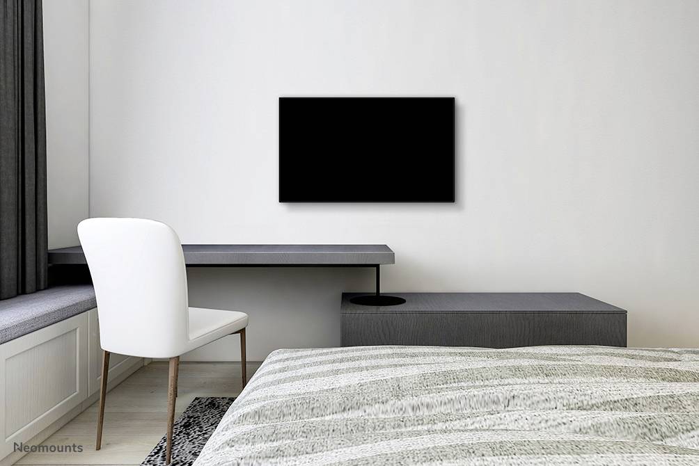 Minimalistická spálňa s posteľou, písacím stolom so stoličkou pri okne a čiernou televíziou na stene.