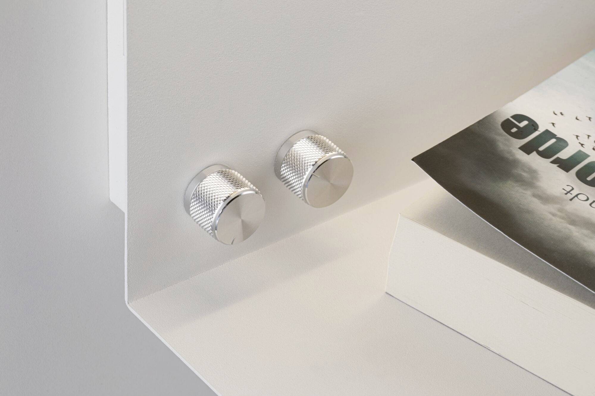 Dva strieborné regulátory na bielom povrchu, vedľa čiastočne viditeľnej brožúry s obrázkom oblohy na obálke.