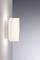 Nástenná lampa s moderným, minimalistickým dizajnom, namontovaná na svetlosivej stene. Jemne svieti smerom nahor a nadol.