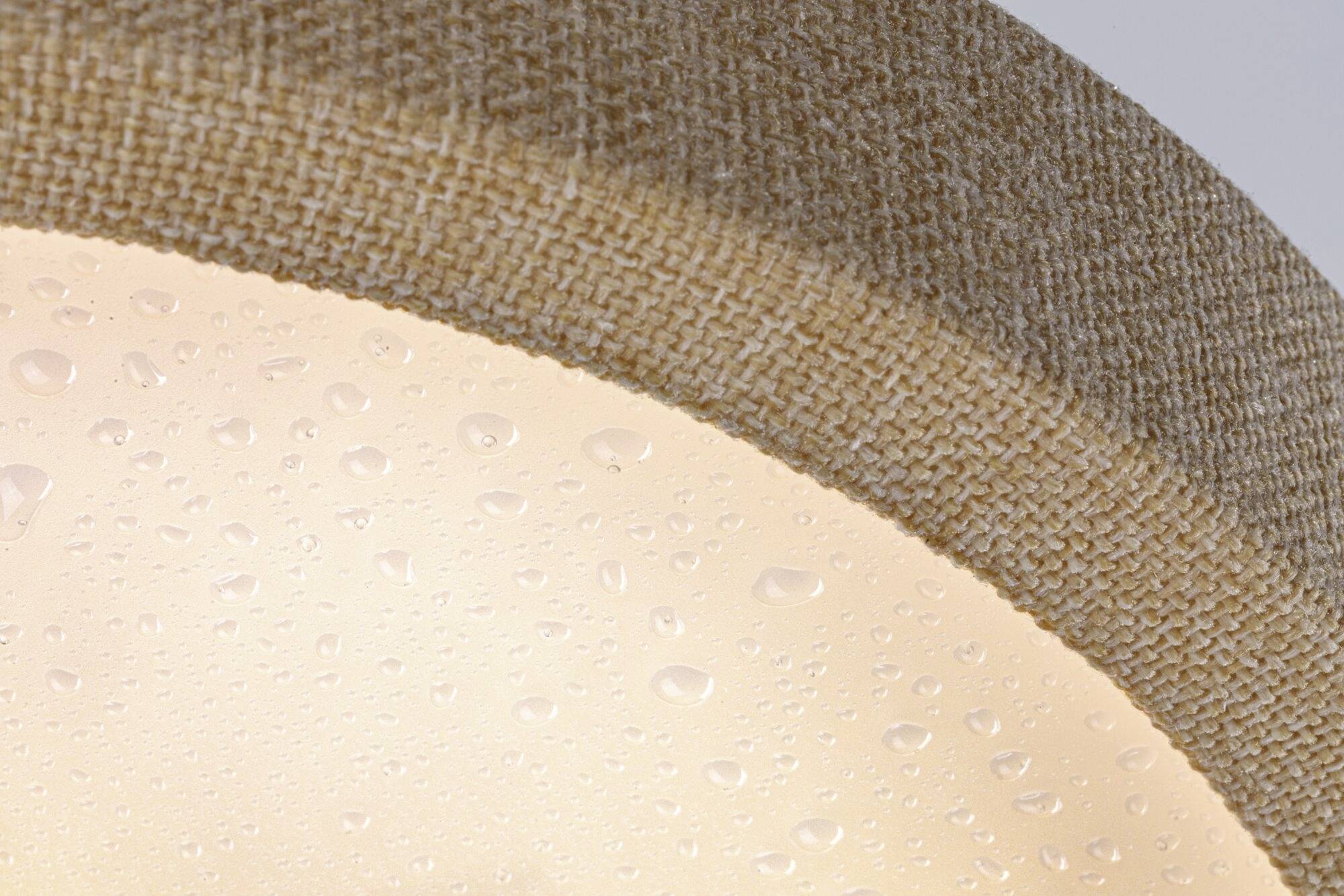 Detailný záber lampy s béžovo-hnedým textilným poťahom a viditelnými kvapkami vody na povrchu.