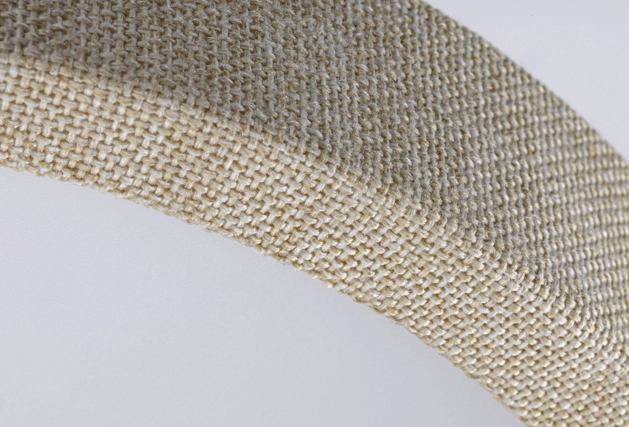 Detail textilného povrchu v béžovej farbe s jemne zvlneným tvarom. Štruktúra tkaniny odhaľuje hustý, tesne tkaný vzor.