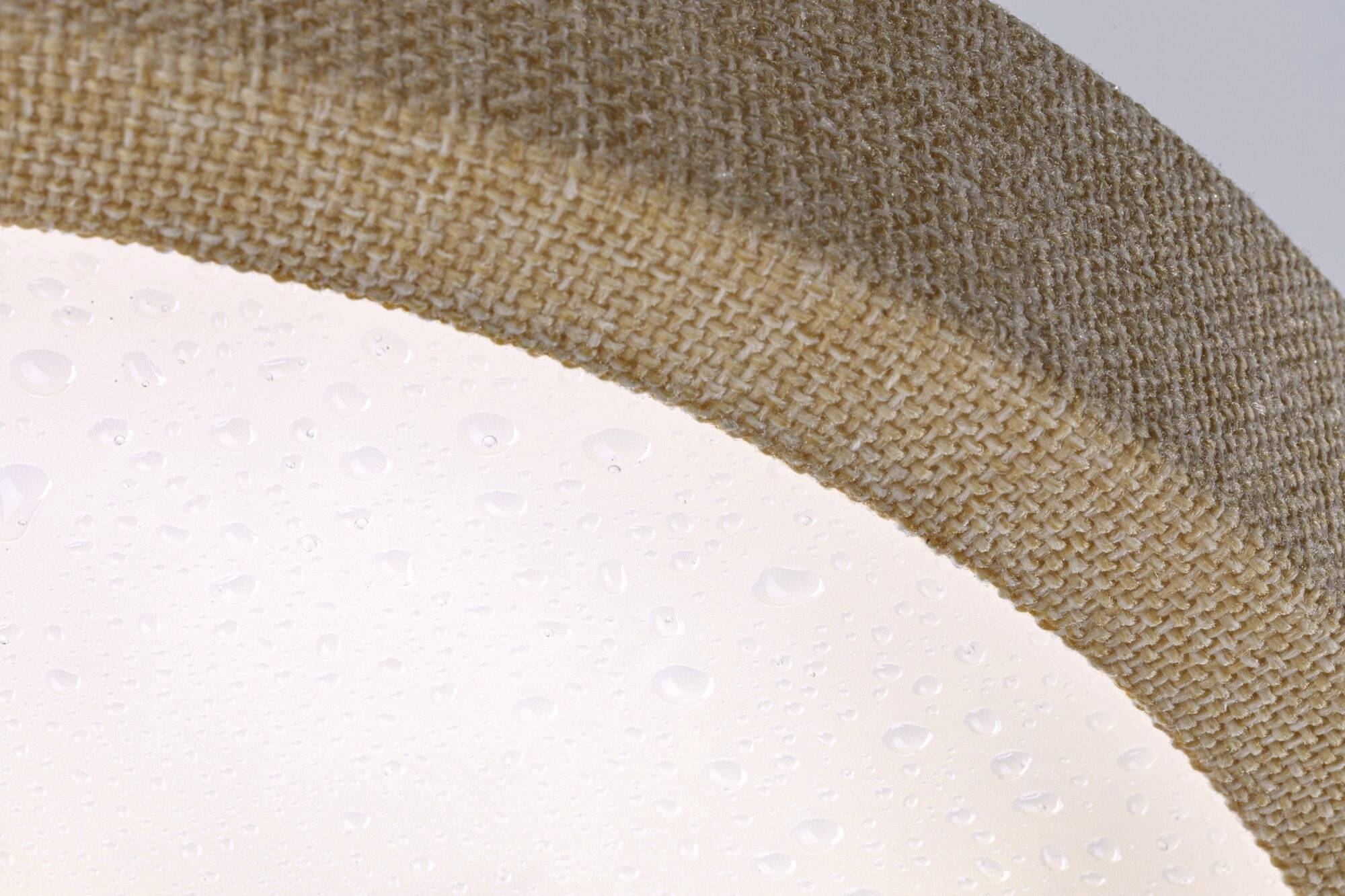 Detailný záber okrúhleho tienidla textilnej lampy s kvapkami vody na povrchu, ktoré zvýrazňujú textúru látky.