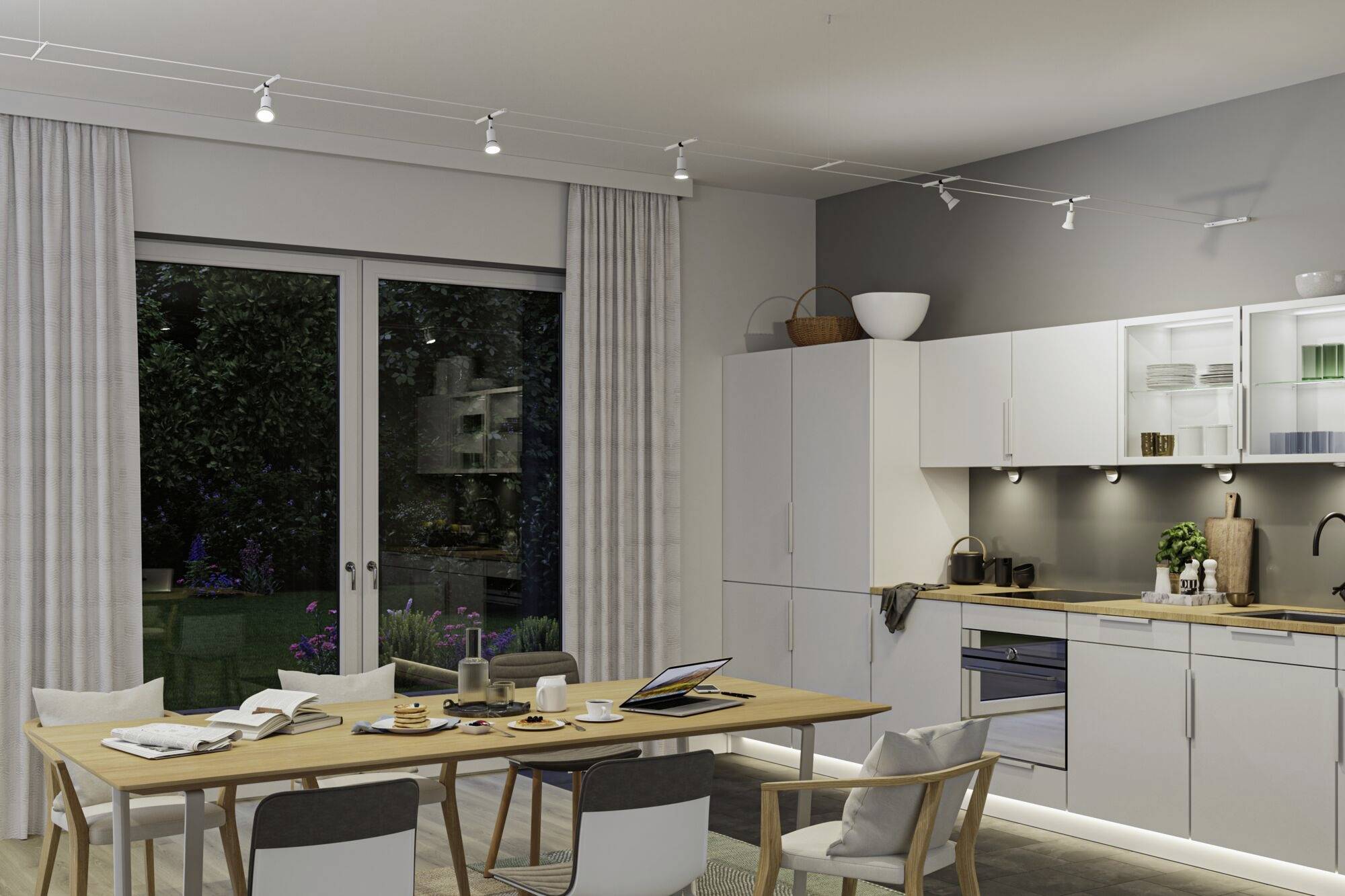 Moderná kuchyňa so stolom, štyrmi stoličkami, laptopom a riadom. Svetlé skrinky, pracovná doska so drezom a spotrebičmi, veľké okná smerujúce do záhrady.