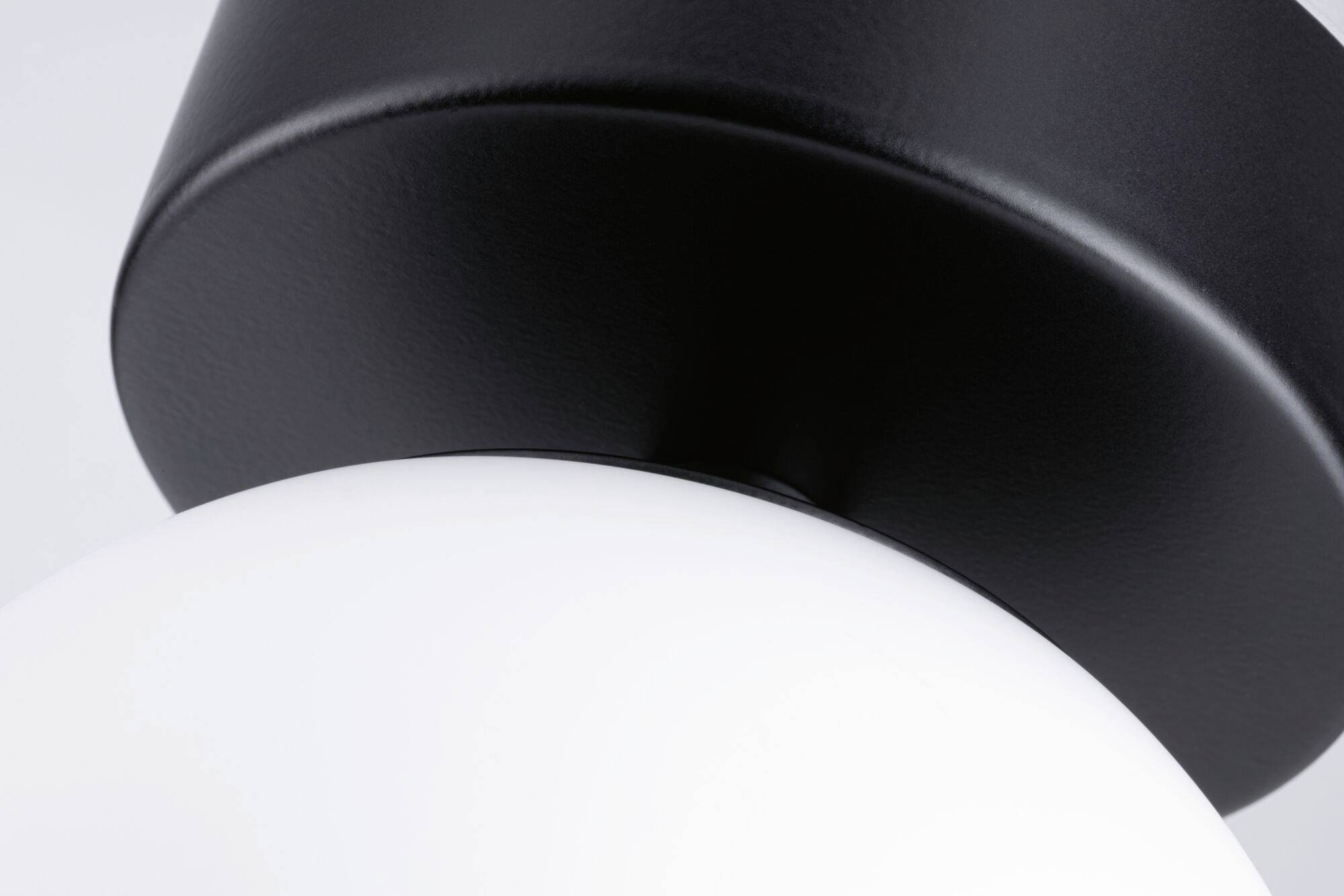 Detailný záber modernej lampy s čiernym kovovým telom a bielou sklenenou kupolou.