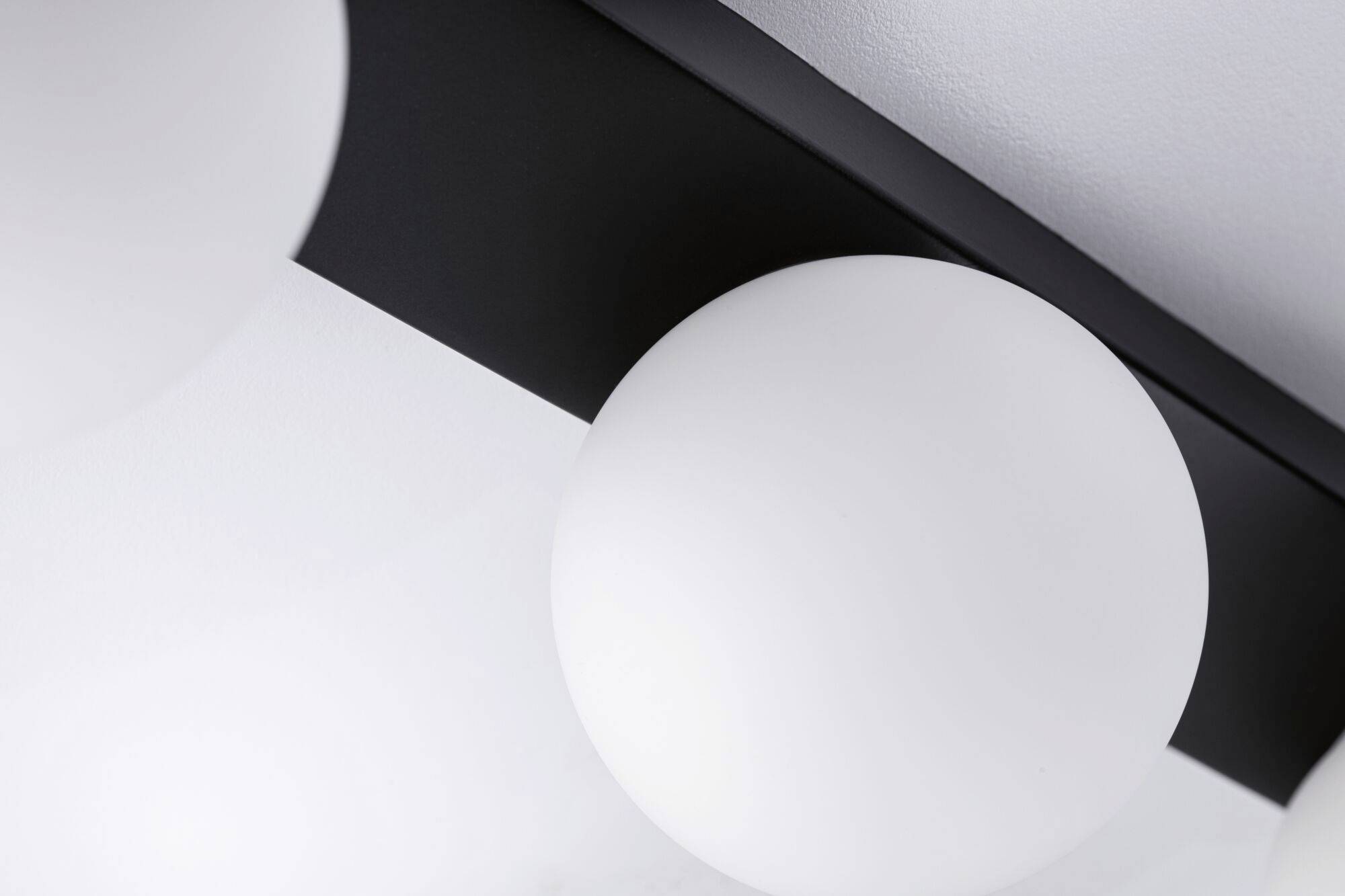 Moderná stropná lampa s guľovitým bielym tienidlom a čiernym držiakom na bielom pozadí.