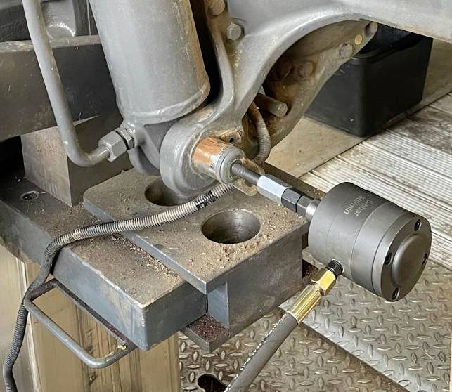 Strojová súčasť s pripojenými hydraulickými vedeniami; znázorňuje možnú údržbu alebo opravu v prostredí dielne.
