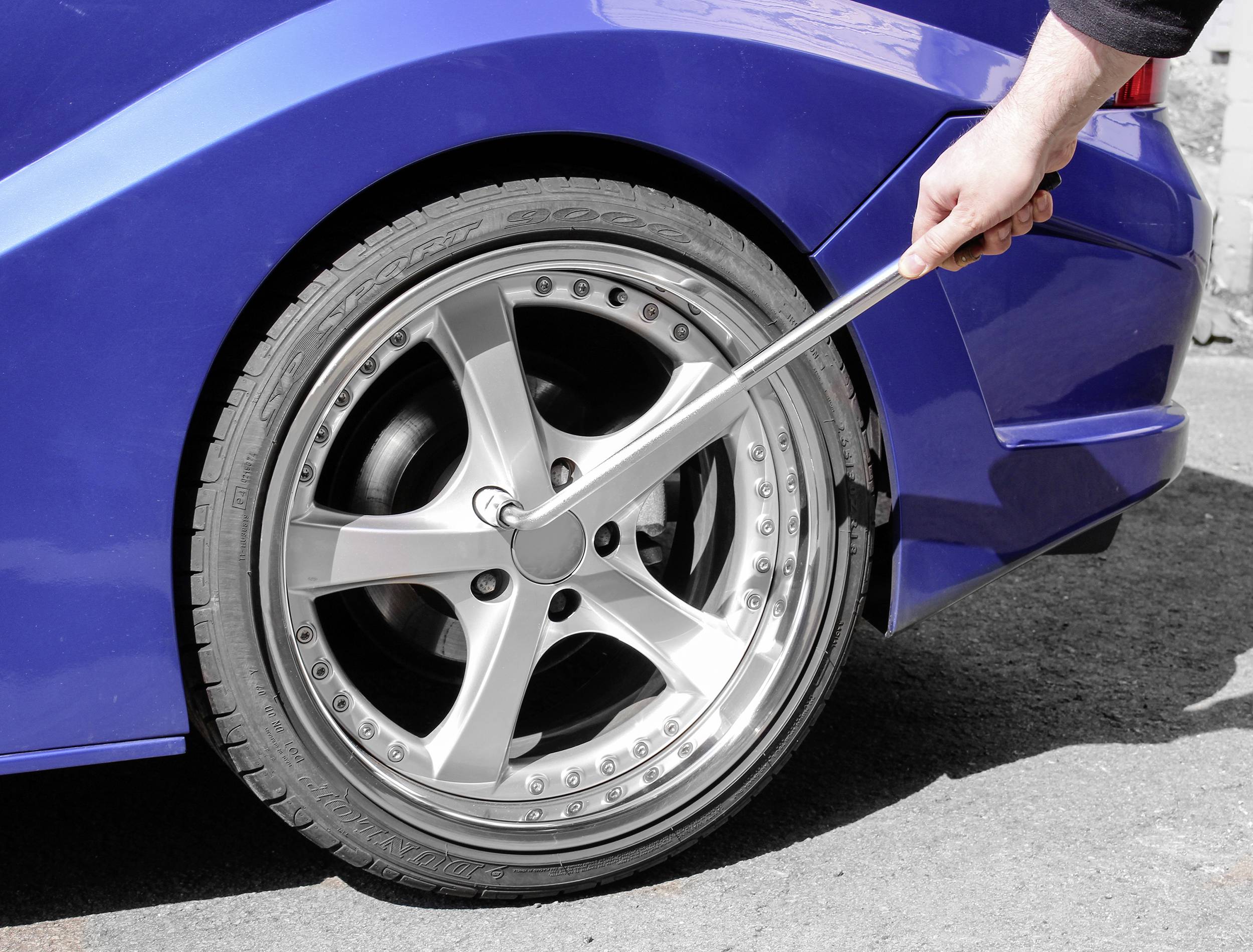 Osoba uťahuje matice na pneumatike automobilu veľkým skrutkovým kľúčom. Vozidlo je modré.