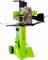 Zelený štiepač dreva na kolieskach, ktorý drží hrubý kmeň stromu vo vertikálnej polohe. Sú viditeľné bezpečnostné výstrahy.