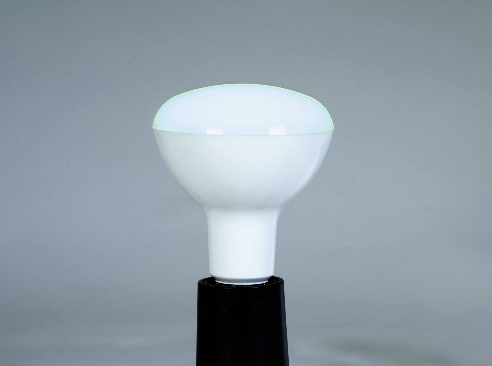 LED lampa s čiernou päticou na sivom pozadí. Lampa je biela a okrúhleho tvaru.