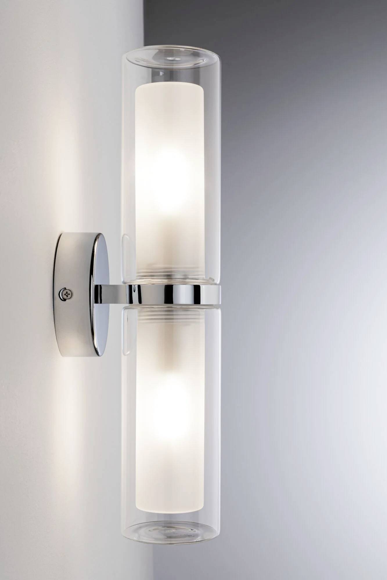 Dvojitá nástenná lampa s valcovitými sklami a kovovým upevnením jasne osvecuje priestor.