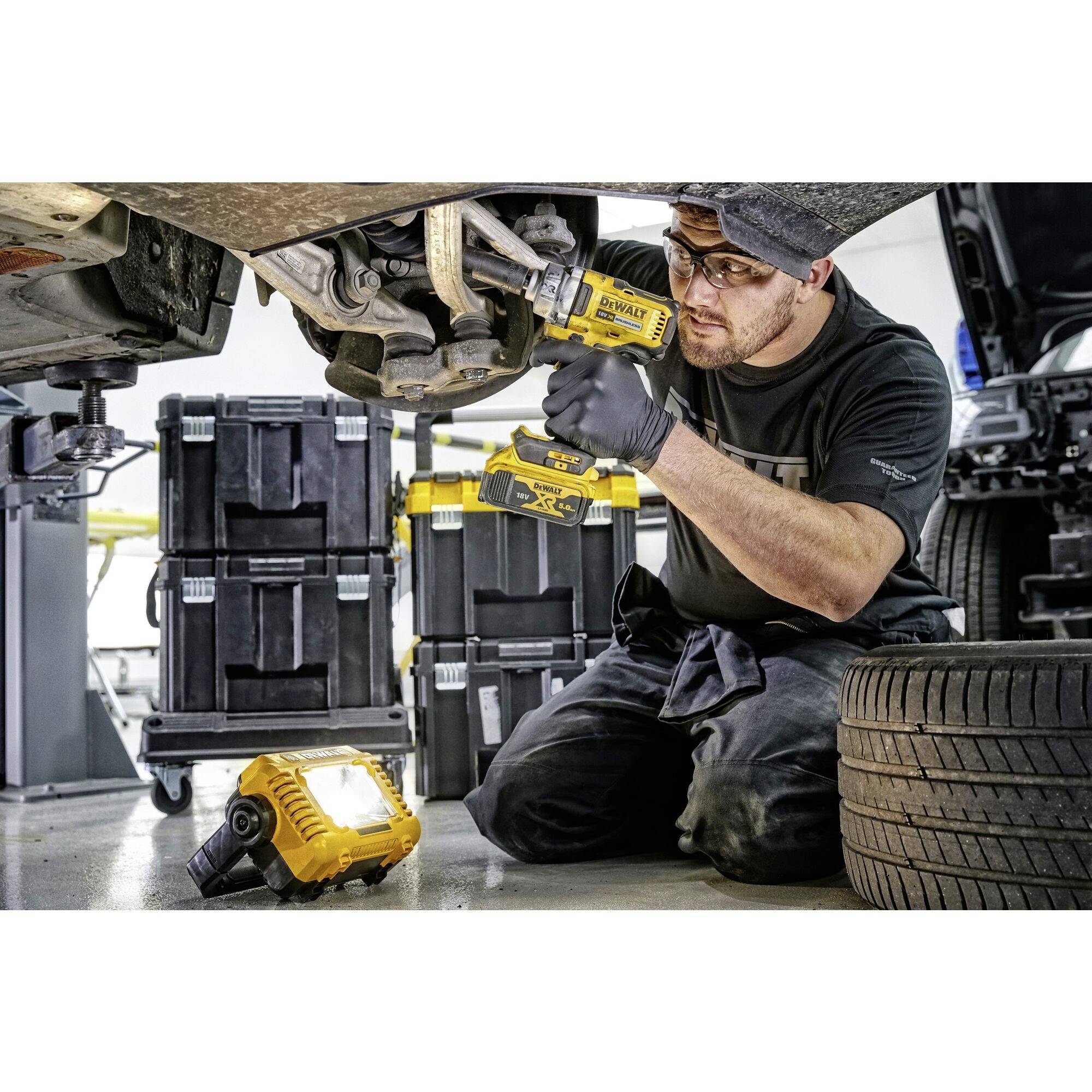 Mechanik vymieňa brzdové doštičky elektrickým náradím pod autom. V pozadí sú viditeľné kufre s náradím.