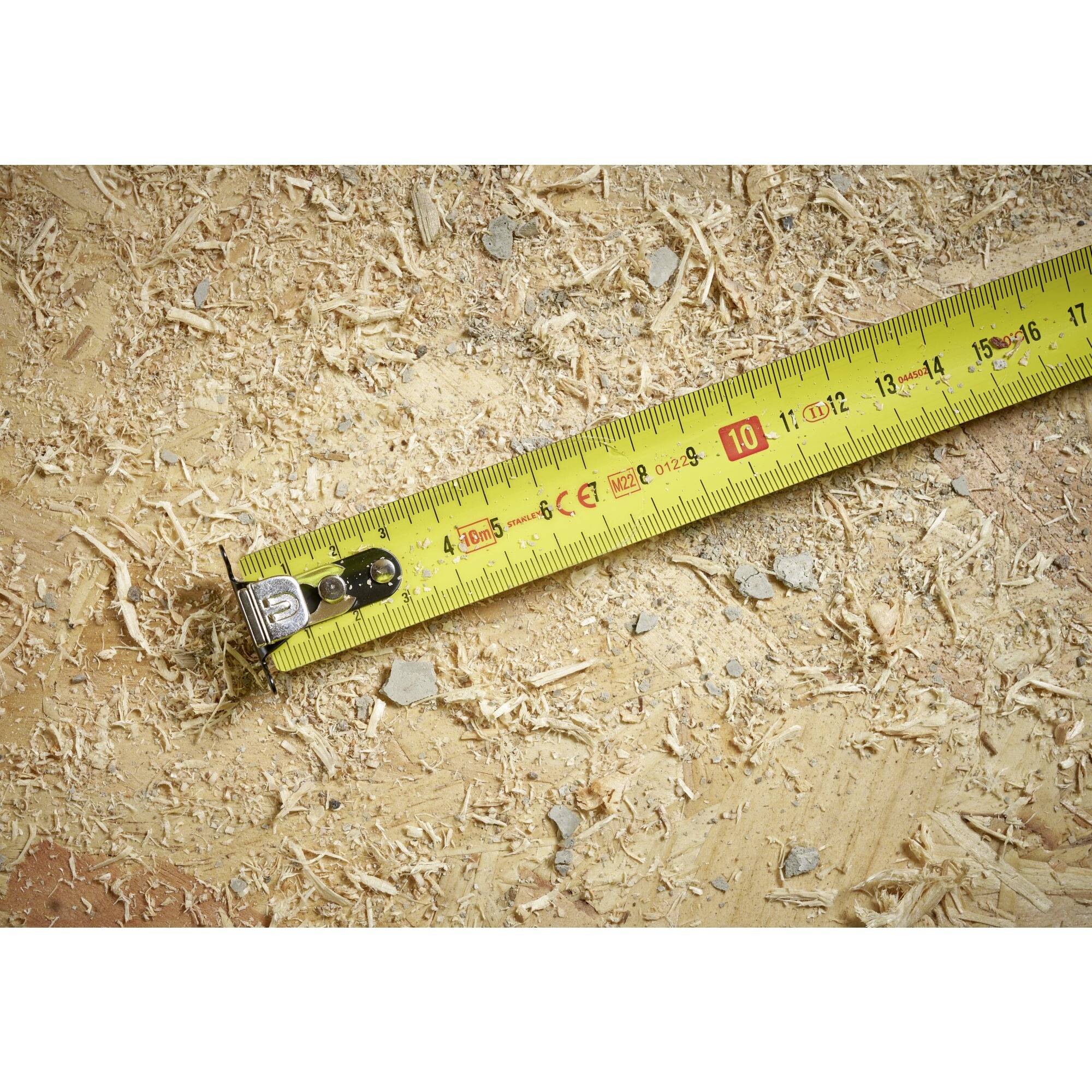 Žltý meter leží na povrchu pokrytom trieskami. Meter je vytiahnutý na 10 cm.