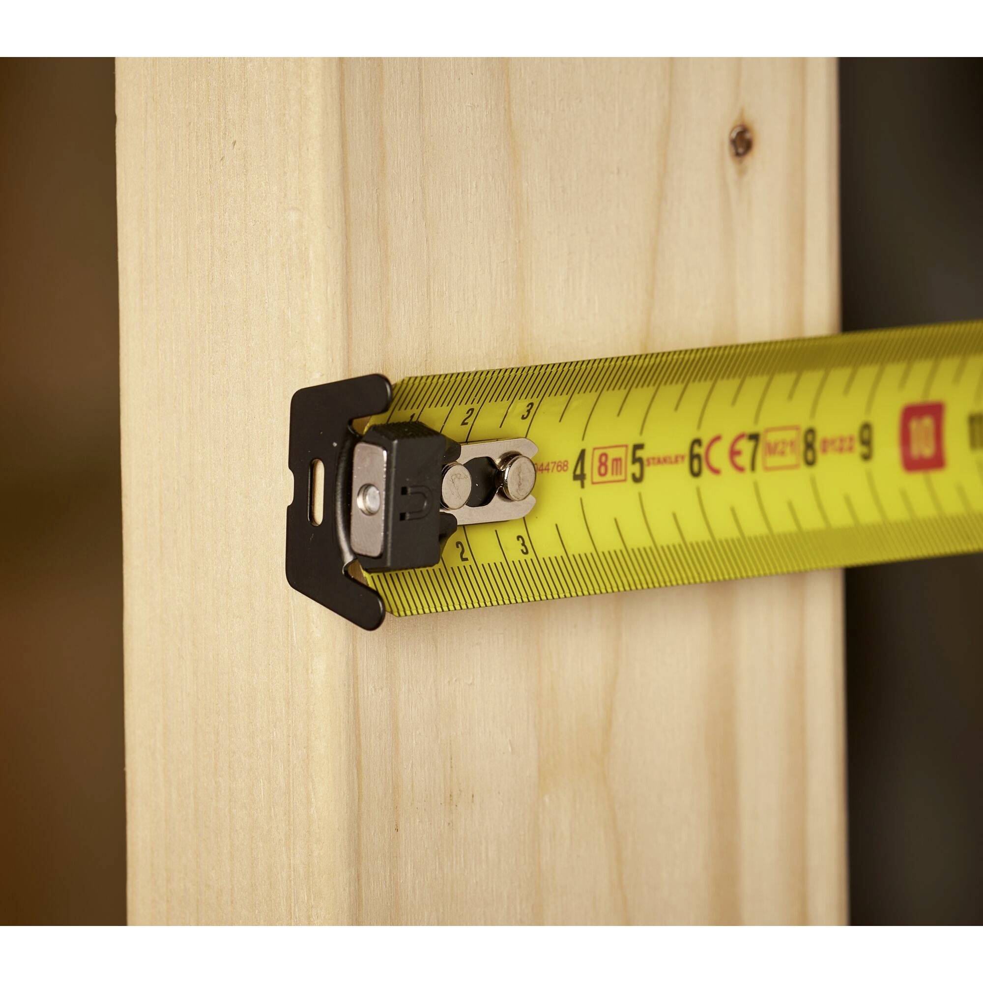 Žltý meter meria šírku drevenej dosky. Meter ukazuje približne 8 centimetrov.