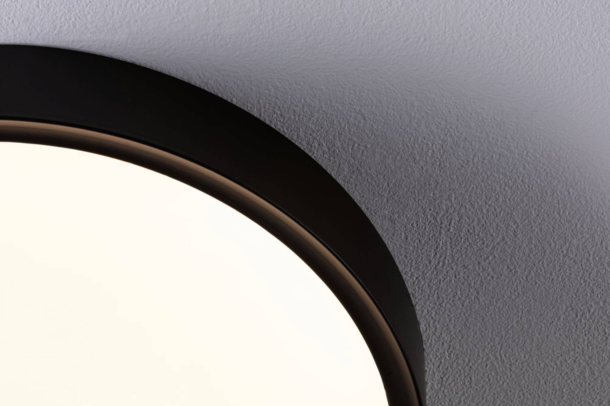 Časť okrúhleho stropného svietidla namontovaného na bielom štruktúrovanom strope. Lampa vytvára jemné, rozptýlené svetlo.