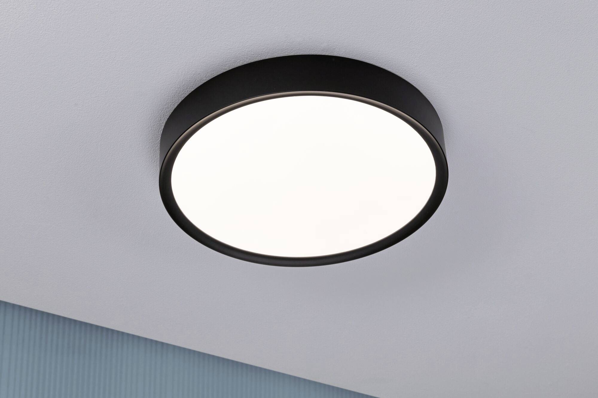 Okrúhle stropné svietidlo s čiernym rámom, namontované na bielom strope, jasne a rovnomerne osvetľuje miestnosť.