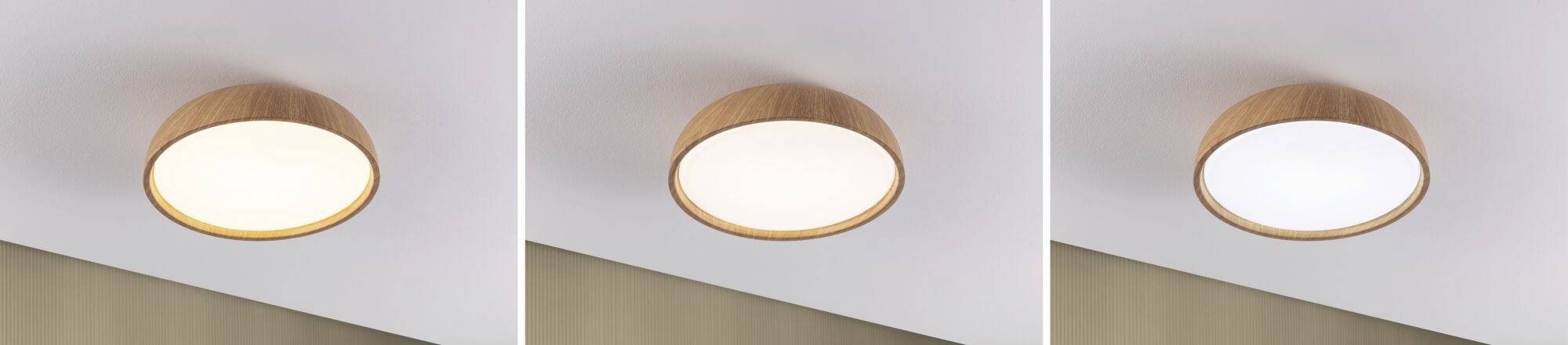 Tri okrúhle stropné svietidlá z dreva s bielym tienidlom, ktoré sa mierne líšia veľkosťou a intenzitou svetla. Upevnené na bielom strope.