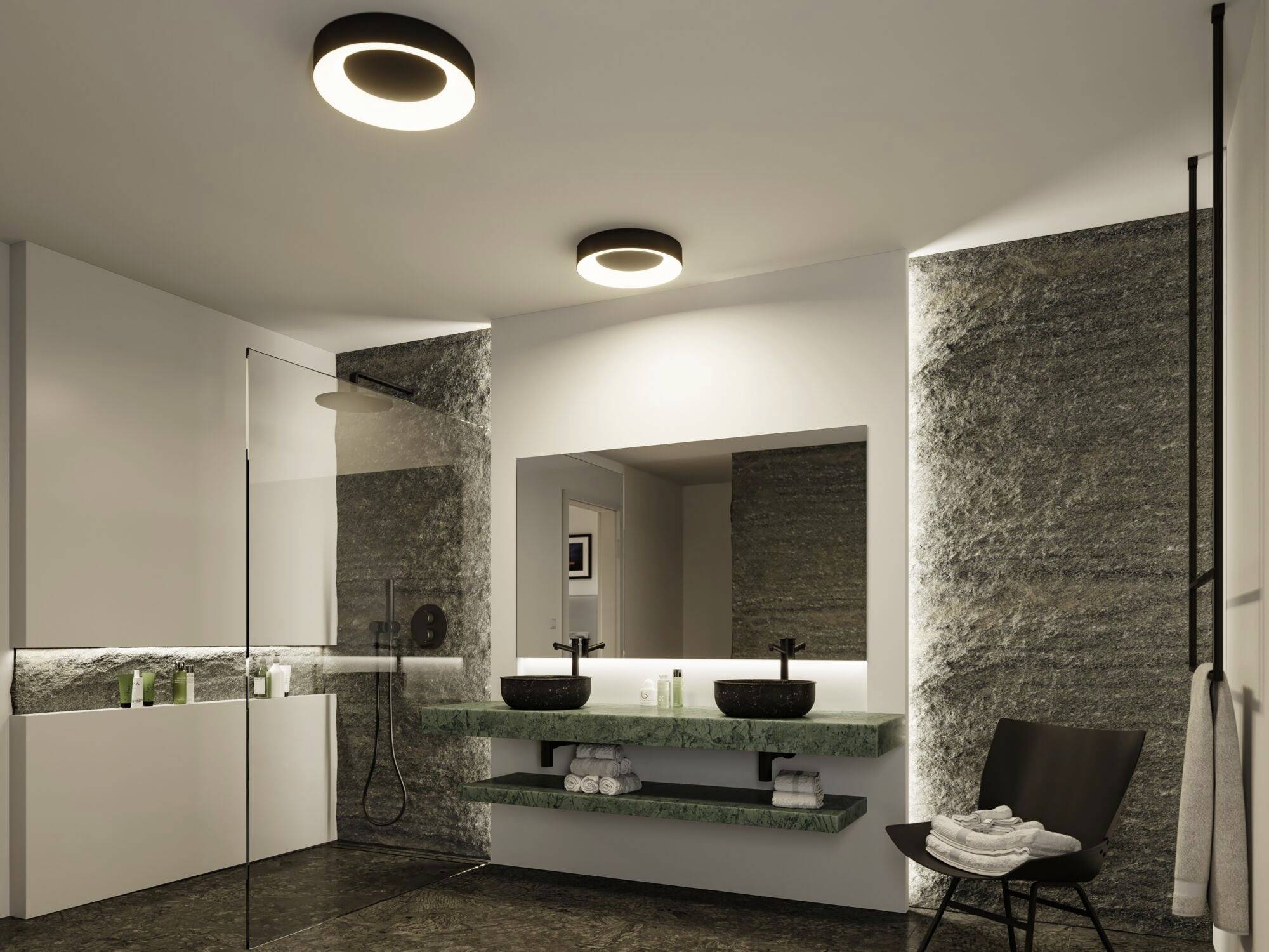 Moderná kúpeľňa s dvoma umývadlami, veľkým zrkadlom a dažďovou sprchou. Steny obložené kameňom a nepriame osvetlenie dodávajú priestoru eleganciu.