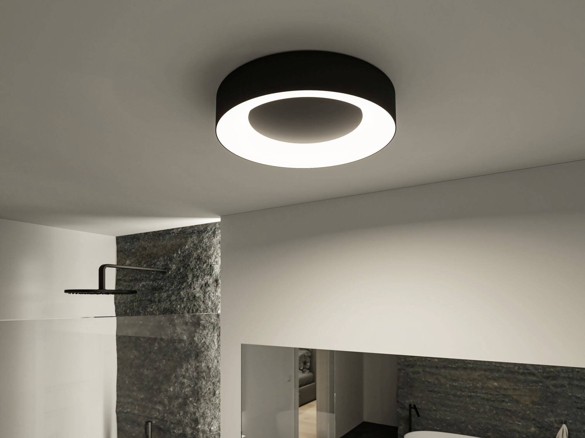 Moderná kúpeľňa s okrúhlym, tmavým stropným svietidlom, ktoré svieti jasným svetlom. Je viditeľná sprcha a časť umývacieho priestoru.