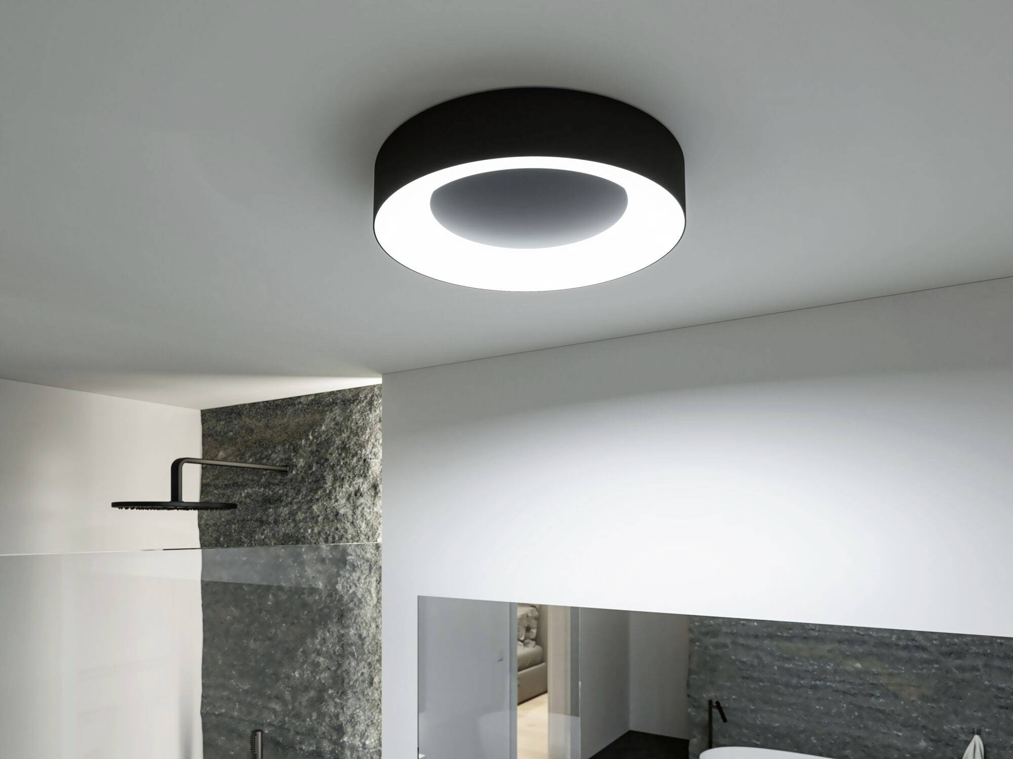 Moderná okrúhla stropná lampa osvetľuje priestor kúpeľne, ktorý zahŕňa dažďovú sprchu a kamenný múr.