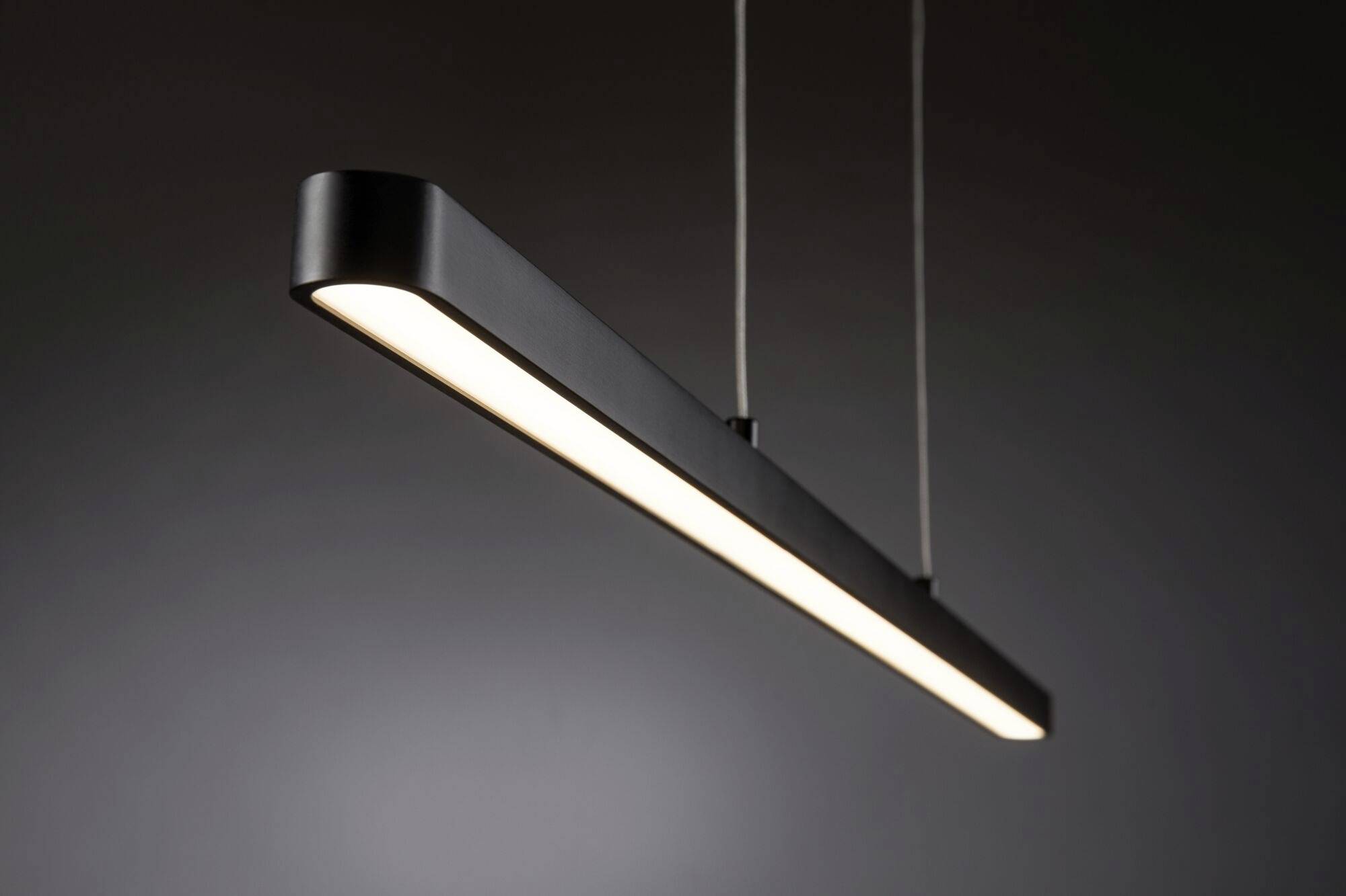 Moderná, obdĺžniková závesná lampa s minimalistickým dizajnom a čiernym povrchom, zavesená pred sivým pozadím. Žiari jasným svetlom.