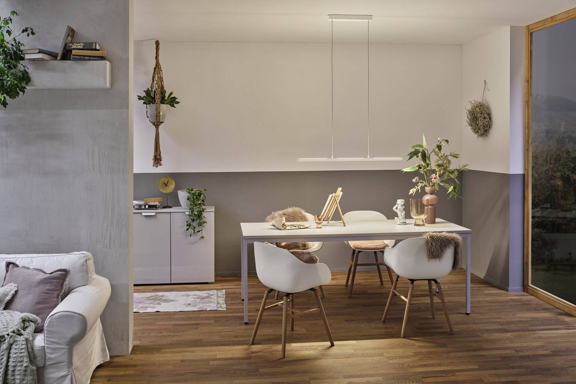 Jedálenská oblasť v modernom štýle s bielym stolom a štyrmi stoličkami na drevenej podlahe. Dekoratívna zeleň a umenie v priestore.