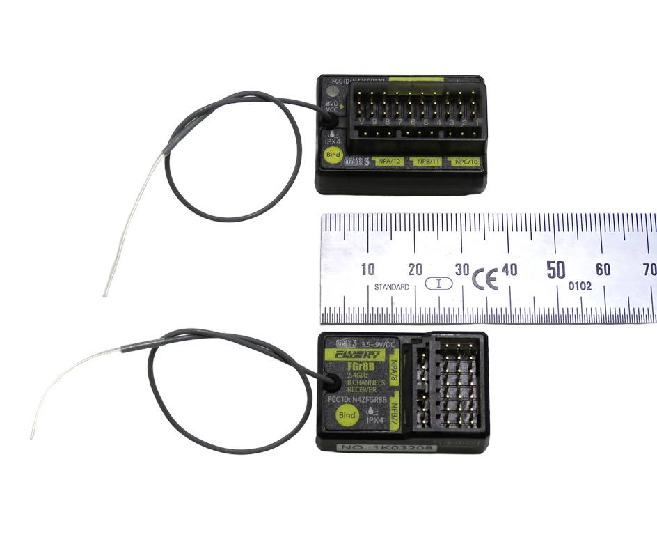 Dva čierne konektory s vodičmi a centimetrová stupnica. Na konektoroch sú viditeľné elektronické obvody.