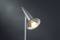 Moderná stojanová lampa s kovovým telom a nakloneným tienidlom svieti v tmavej miestnosti.