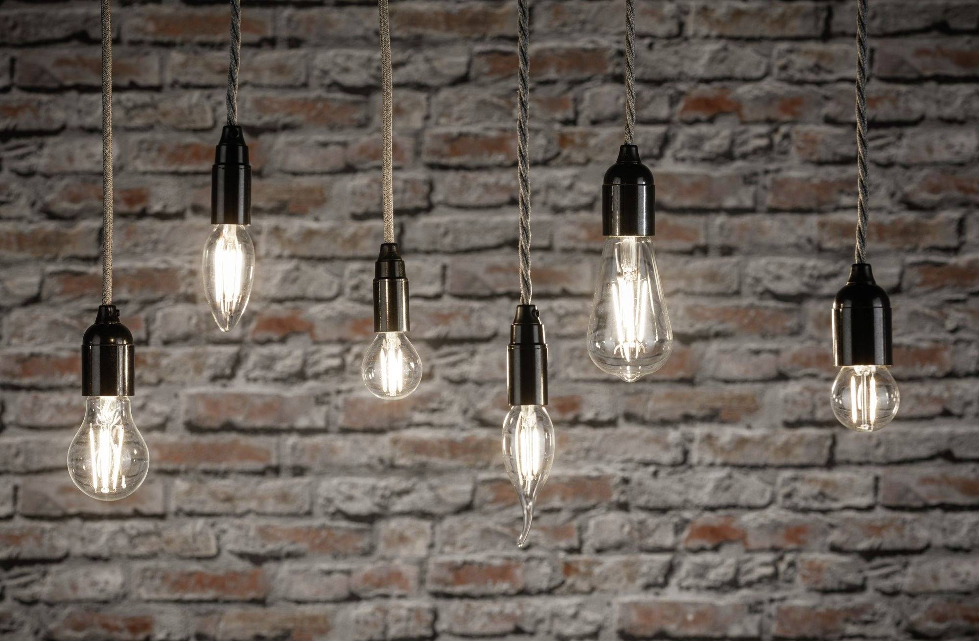 Šesť visiacich žiaroviek pred červenou tehlovou stenou.