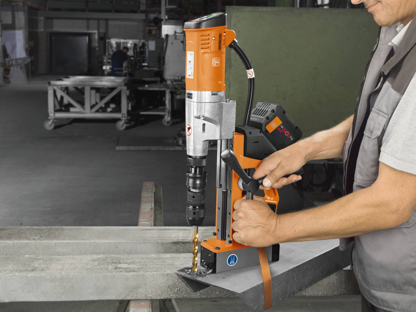 Osoba obsluhuje magnetickú vŕtačku v dielni, aby presne navŕtala diery do kovového nosníka.