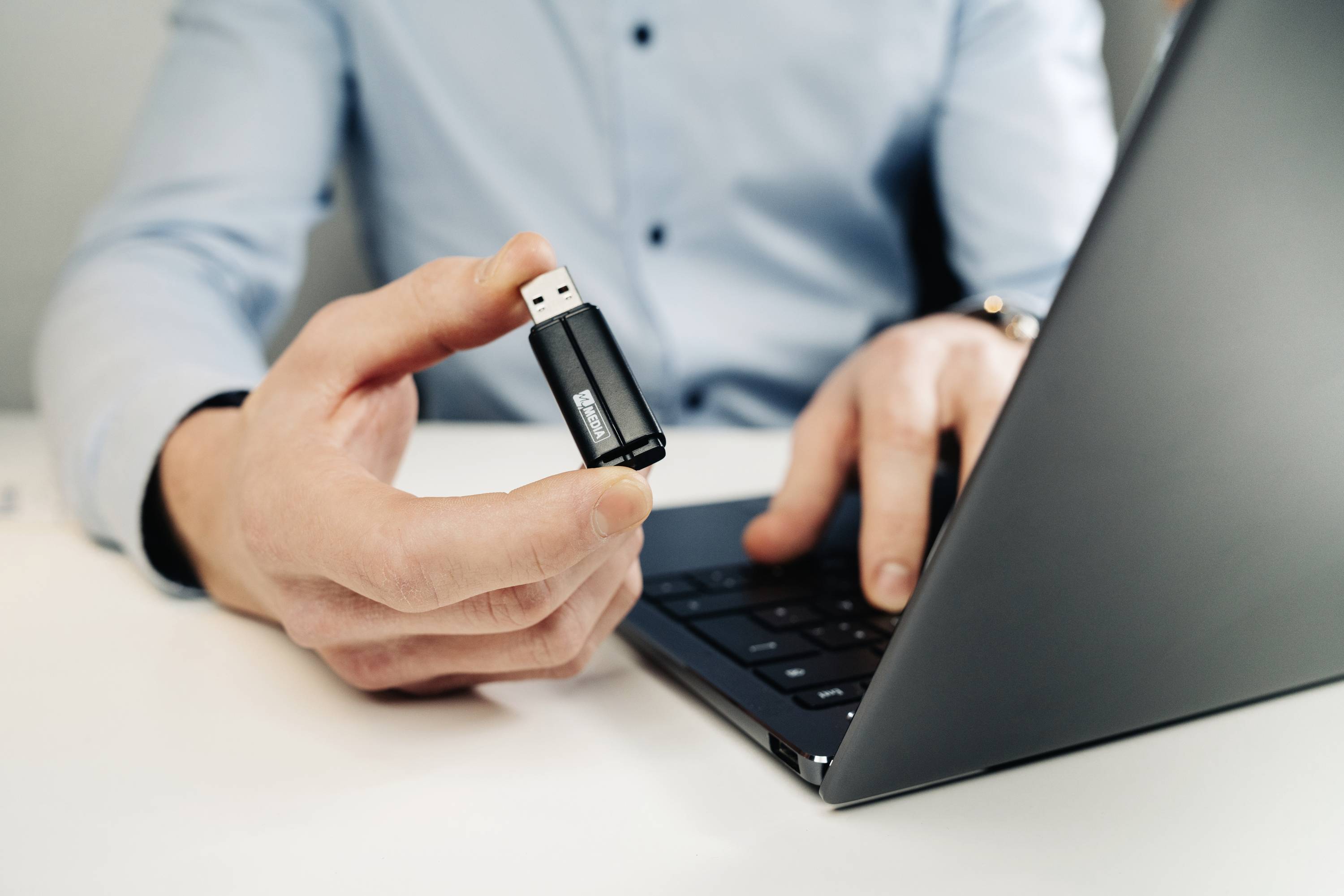 Osoba drží USB kľúč nad laptopom, pripravená ho zapojiť. Technológia v práci.