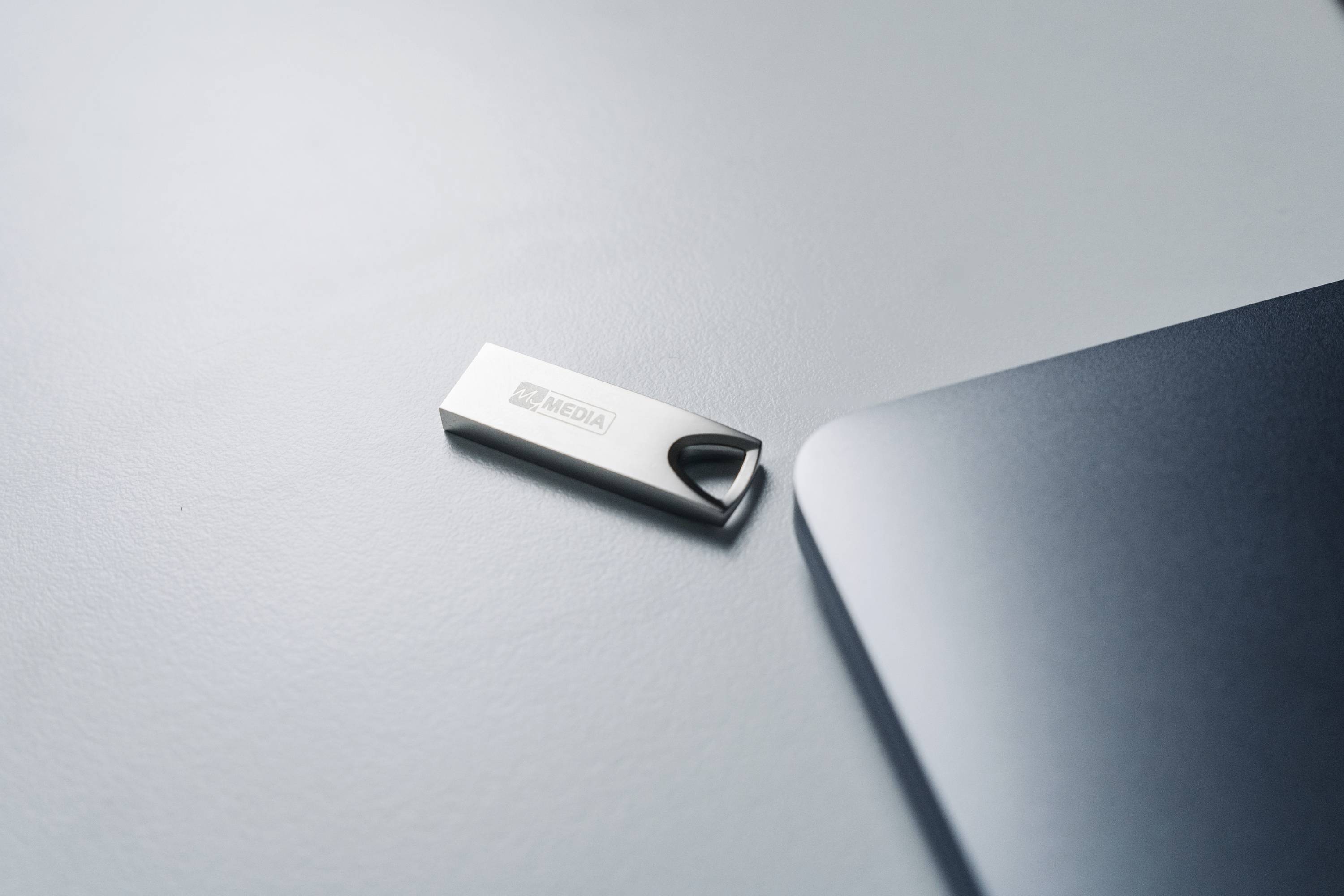 USB kľúč leží vedľa laptopa na písacom stole.