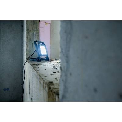 Stavenisková lampa osvetľuje zošúverené okenné prkno v opustenom priestore. Prach a sutiny sú viditeľné.
