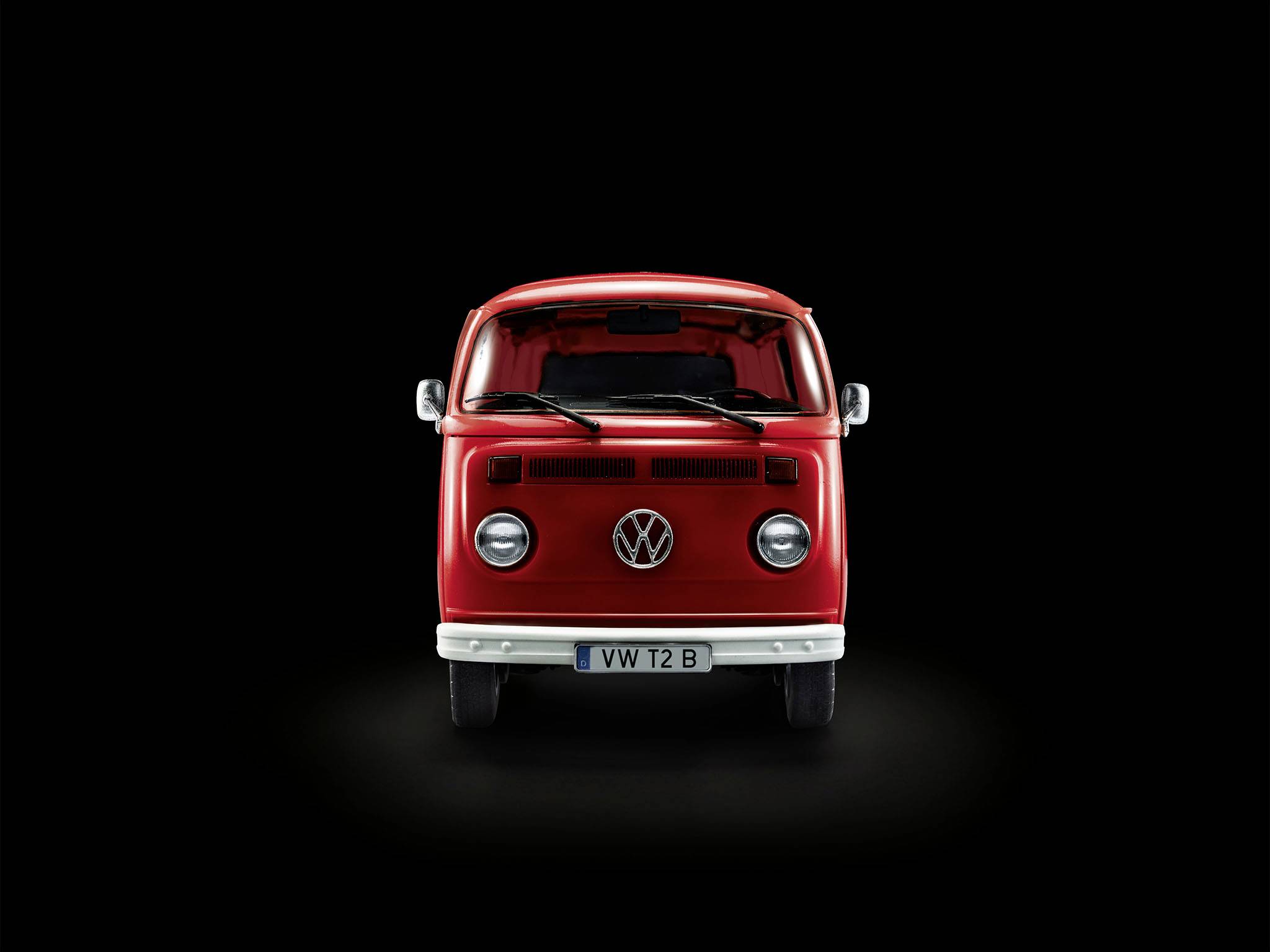 Červený Volkswagen-Bus T2, pohľad spredu na čiernom pozadí. Autobus má okrúhle svetlomety a charakteristické logo VW.