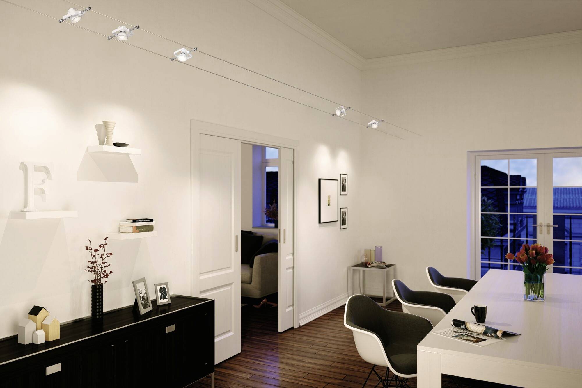 Moderná obývacia izba s bielymi stenami, čiernou príborníkom, jedálenským stolom a stoličkami, dekorovaná vázami a rámikmi na fotografie.