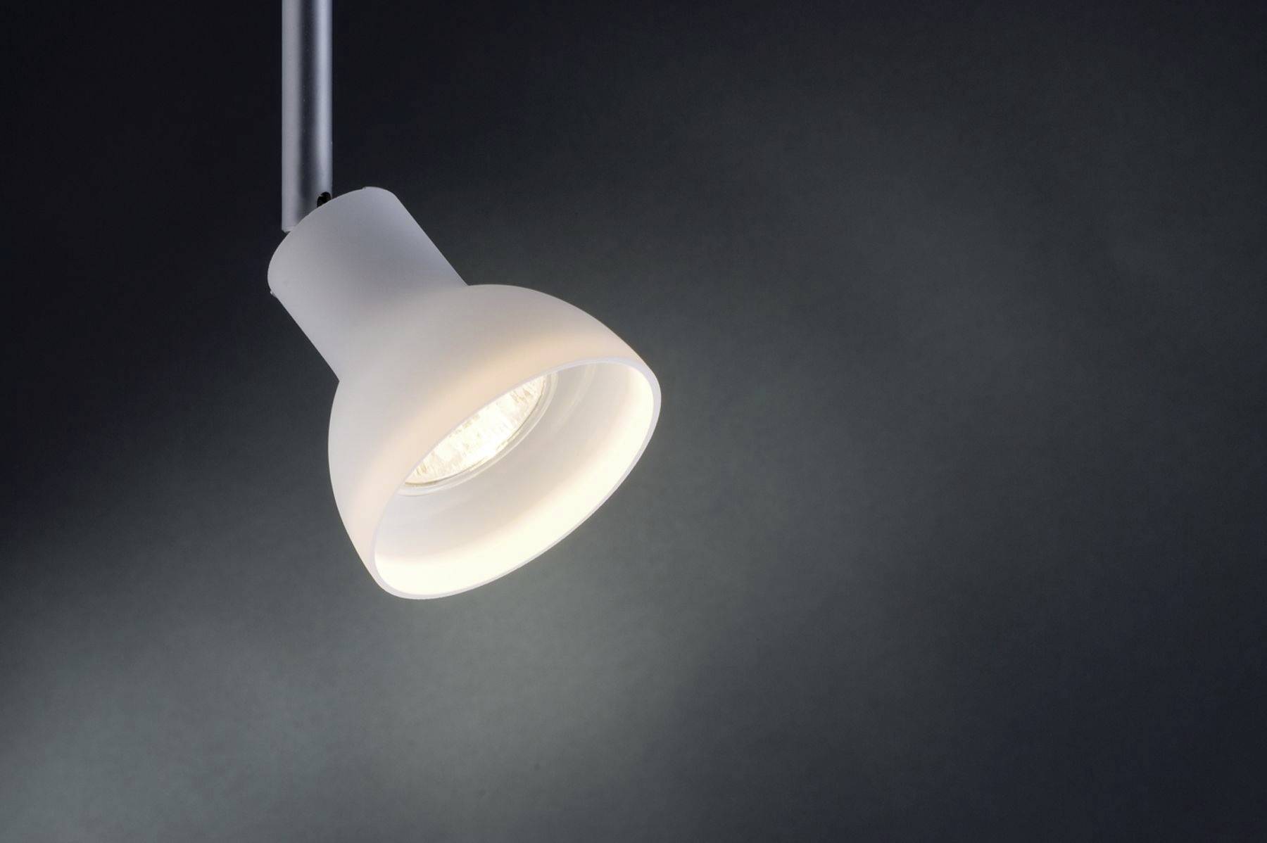 Jedna biela stropná lampa svieti oproti tmavému pozadiu.