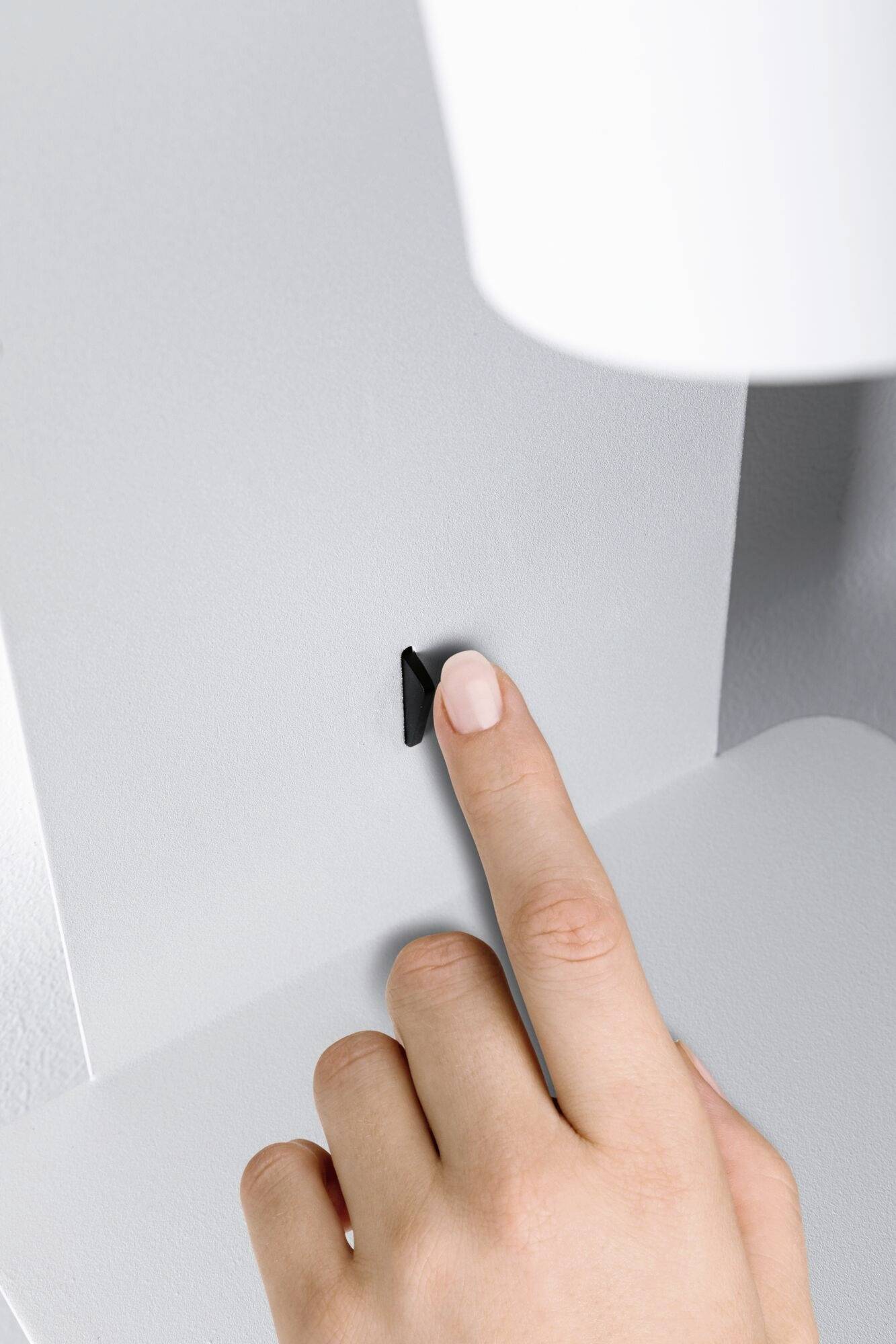 Ruka stláča malý čierny prepínač na bielej stene alebo zariadení.