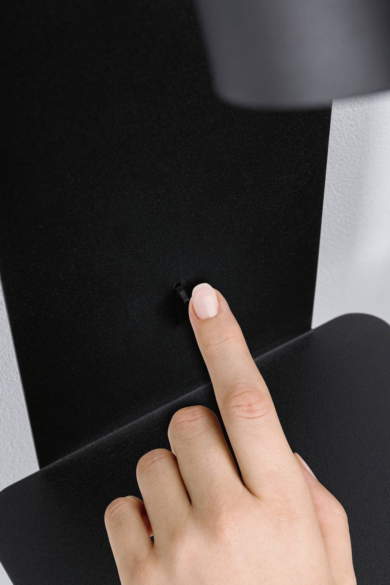 Ruka sa dotýka malého čierneho tlačidla na matne čiernom povrchu.