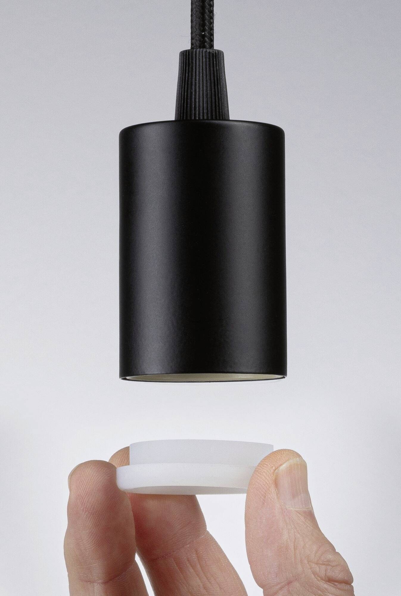 Čierny valcovitý tienidlo sa vznáša nad rukou, ktorá drží malý, guľatý, biely predmet.