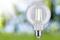 Žiarovka svieti na slnku pred rozmazaným zeleným pozadím a symbolizuje energiu a inováciu.