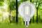 LED žiarovka vznášajúca sa pred slnkom zaliateným lesom symbolizuje ekologickú energiu a spätosť s prírodou.