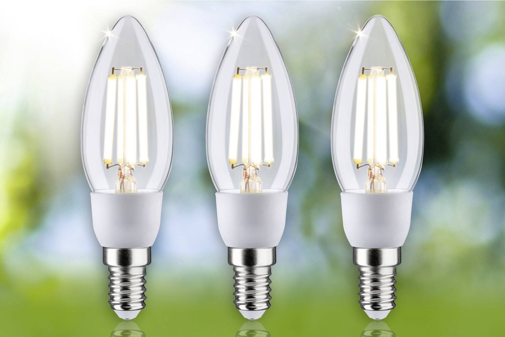 Tri LED lampy v tvare sviečok so viditeľnými vláknami, zoradené pred rozmazaným pozadím. Energeticky úsporná možnosť osvetlenia.