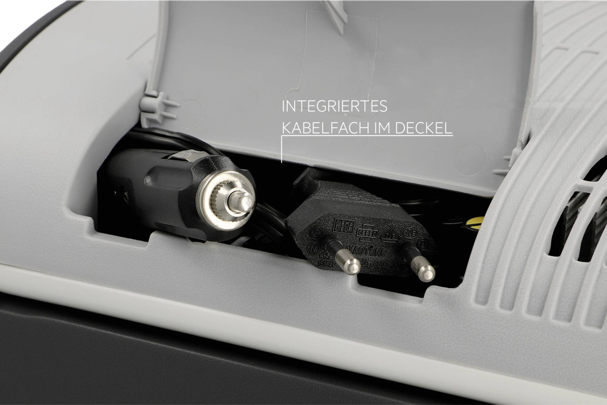 Integrovaný kábelfach s eurozásuvkou a automobilovým nabíjacím adaptérom v sivom kryte.
