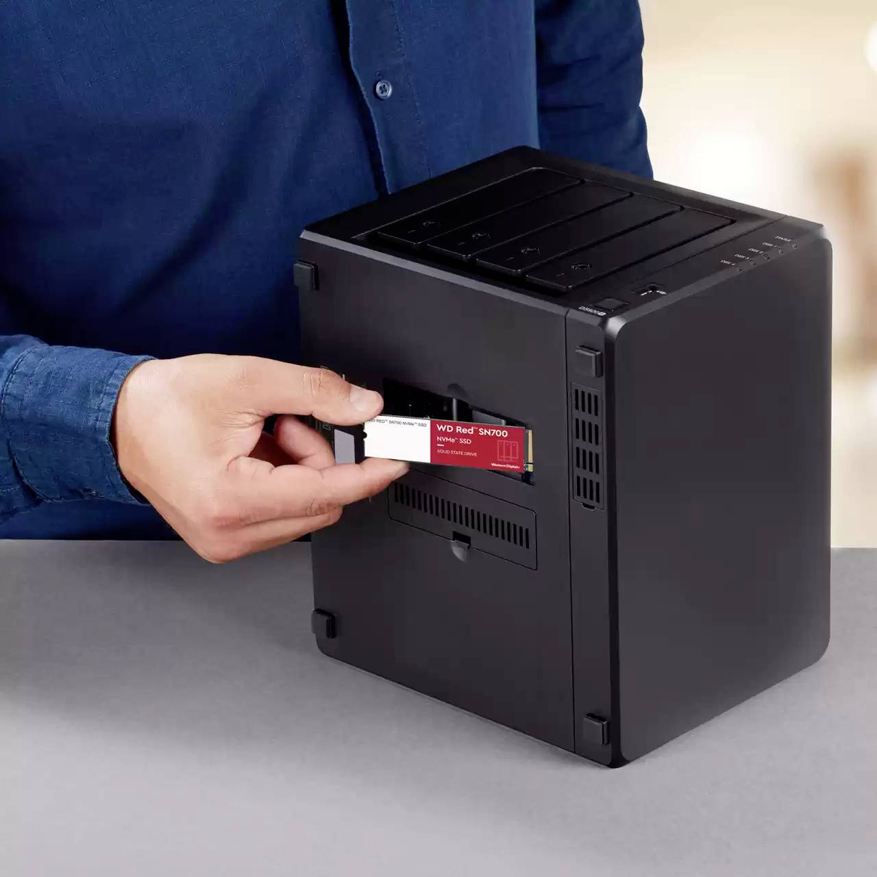 Osoba inštaluje červený úložný disk WD Red SA500 NAS do čiernej skrinky na sivom stole.