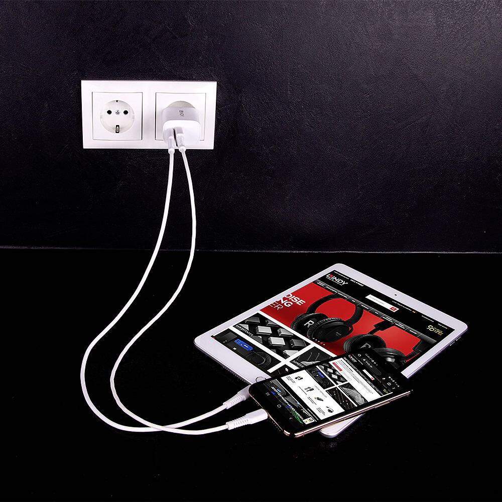 Tablet a smartfón sú nabíjané cez nabíjacie káble do elektrickej zásuvky. Na tablete je otvorená nákupná webová stránka so slúchadlami.